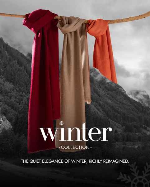 A clean, high-contrast creative featuring three colorful scarves hanging against a grey mountain backdrop to evoke seasonal elegance.