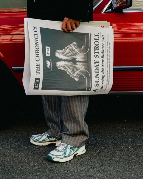 A lifestyle-focused creative featuring a model holding a branded newspaper showcasing the running shoe, styled with tailored trousers for an editorial look.