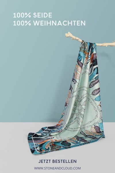 A minimalist studio shot of a patterned silk scarf hanging from a natural branch against a serene blue background.