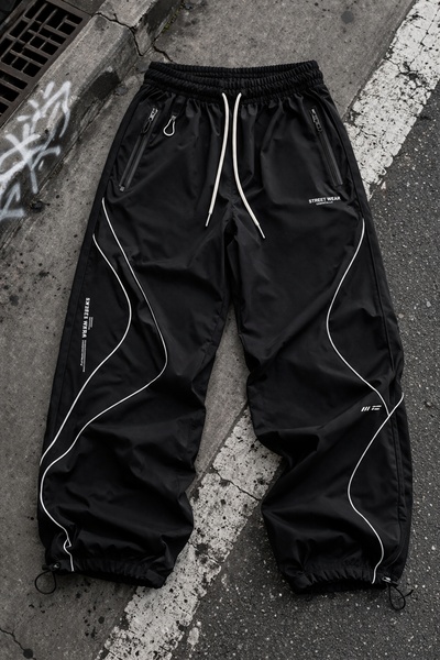 A high-contrast, overhead studio shot of technical black cargo pants with reflective piping details, styled for a modern urban aesthetic.