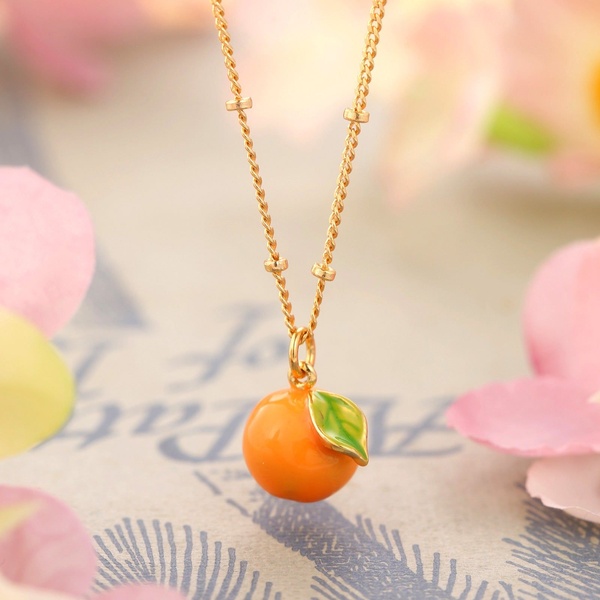 A clean, centered close-up shot of a delicate orange charm necklace, highlighting its vibrant color and fine chain details.