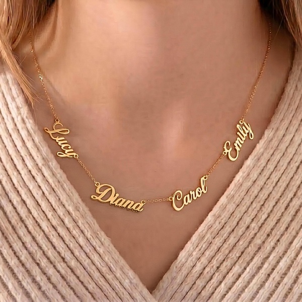 A close-up, high-quality product shot of a personalized name necklace featuring multiple names on a delicate gold chain worn by a model.