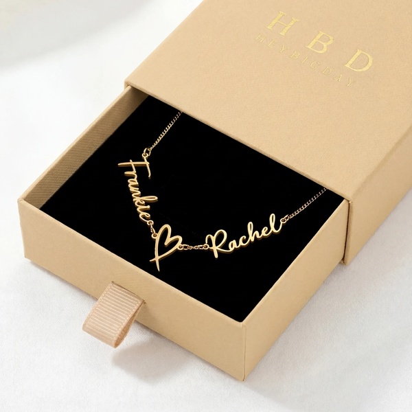 A high-end, clean-focused product hero shot featuring a gold custom name necklace displayed in an open gift box.