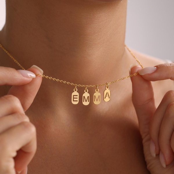 A close-up, high-key shot showing a personalized gold necklace being adjusted by a model to highlight the name charms.