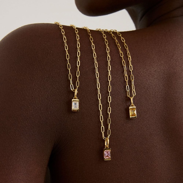A close-up, high-fashion studio shot showcasing three gold pendant necklaces resting on a model's shoulder.