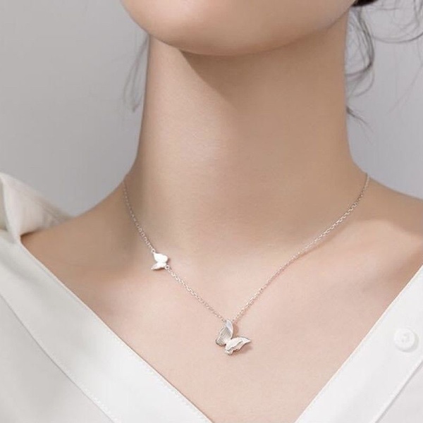 A close-up, high-key shot focusing on a delicate silver butterfly necklace worn by a model, emphasizing clean lines and elegant simplicity.