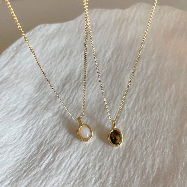 A high-end, clean product shot featuring two delicate gold necklaces with stone pendants on a textured white background.