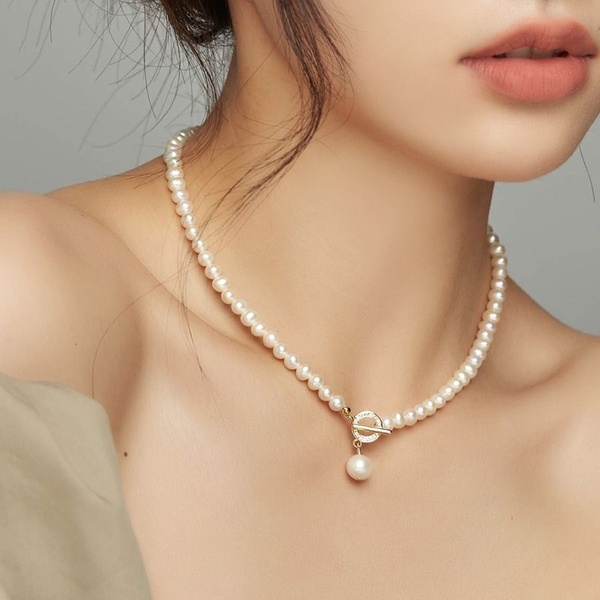 A close-up portrait of a woman wearing a simple pearl necklace with a toggle clasp, focusing on elegance and product details.