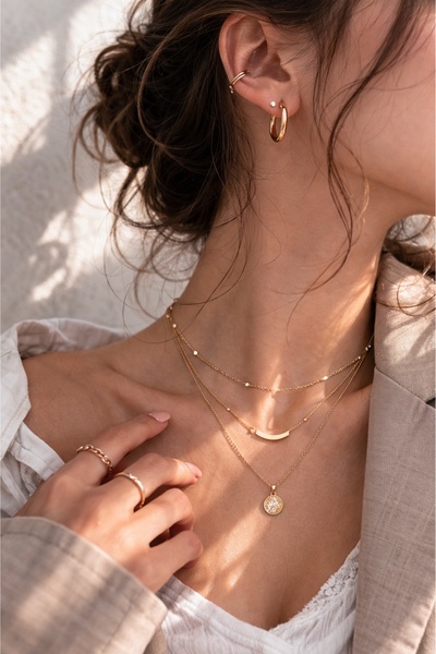 A close-up lifestyle shot focusing on the delicate layering of gold necklaces on a model, emphasizing elegance and high-end jewelry styling.