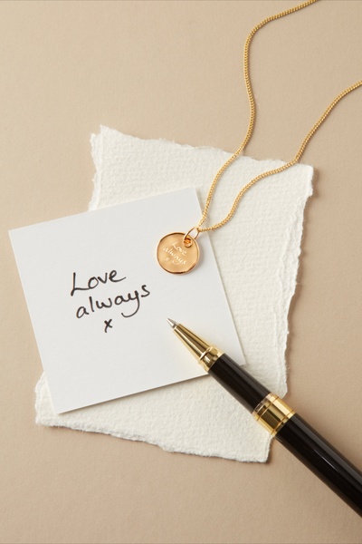 A close-up of a gold necklace with a handwritten 'Love always' note on paper, emphasizing personal sentiment and delicate aesthetics.