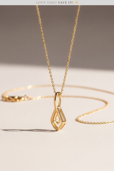 A high-end, clean product shot of a gold pendant necklace on a neutral studio background, emphasizing texture and refined lighting.