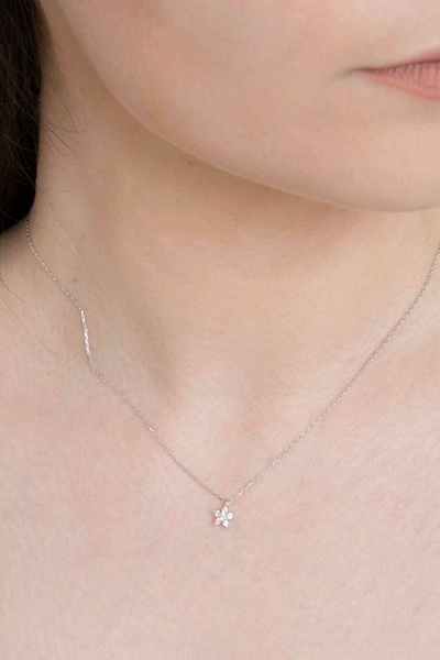 A close-up, high-detail shot of a delicate silver flower pendant necklace worn on a model to showcase product elegance.