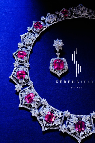 A high-contrast, studio-lit hero shot of a luxury necklace and matching earring, featuring deep blue backdrops and vibrant pink gemstone accents.