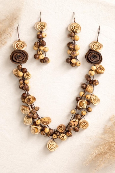 A high-quality studio shot of a handcrafted necklace and matching earrings featuring wood-like beads and spiral accents on a neutral textured background.