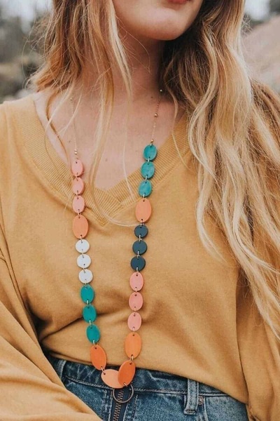 A close-up lifestyle photograph focusing on a vibrant, multi-colored wooden bead necklace worn against a simple mustard-toned top.