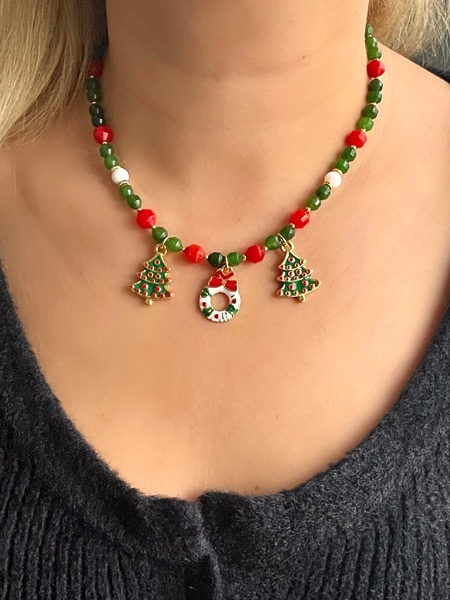 A close-up, high-angle portrait shot featuring a model wearing a festive beaded necklace with holiday-themed tree and wreath charms.