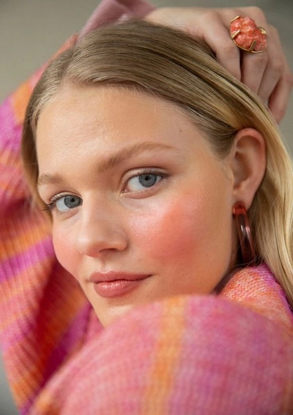 A close-up portrait of a woman wearing a statement ring and hoop earrings, focusing on a natural and soft-toned aesthetic.