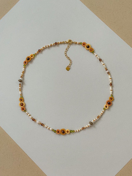 A close-up product shot of a delicate, handcrafted beaded flower necklace on a clean, neutral background highlighting its artisanal charm.