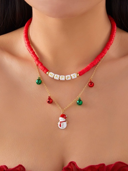 A close-up studio shot of a festive holiday necklace featuring a snowman charm, red clay beads, and bells against a neutral background.