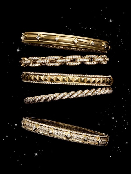 A high-end, vertically stacked composition of five distinct gold and diamond bracelets floating against a starry black background.