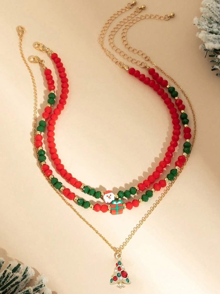 A close-up product photo of a three-layer Christmas necklace featuring red and green beads, a Santa Claus charm, a gift charm, and a tree pendant.