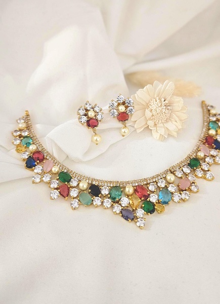 A high-quality, static studio product shot of a multi-color statement necklace and matching earrings placed on a soft, draped white fabric.