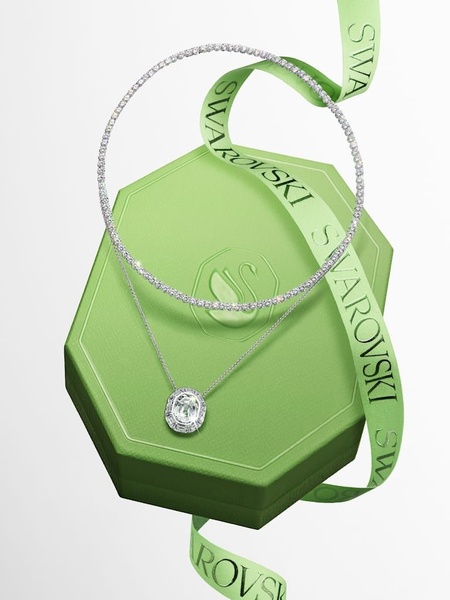 A high-end studio shot of a necklace and pendant draped over a branded gift box, featuring a floating, ethereal composition.