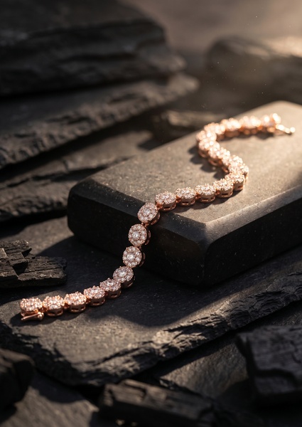A close-up photograph of a rose gold tennis bracelet resting on a dark slate surface, illuminated by warm, directional golden hour lighting.