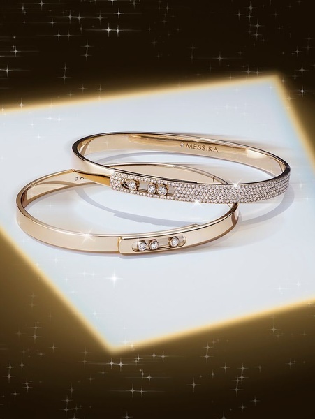 Two elegant gold bracelets are displayed on a clean white platform under a warm, sparkling glow, emphasizing luxury and precision.