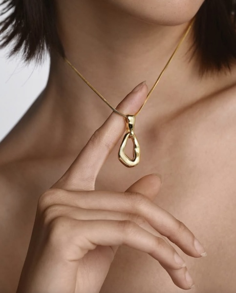 A close-up shot of a model wearing a unique gold pendant necklace, highlighting the intricate texture and high-end finish of the jewelry.