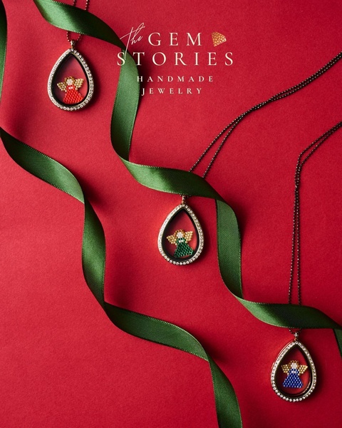 This holiday-themed creative features three handmade angel-shaped pendants arranged on a rich red background with flowing green silk ribbons.