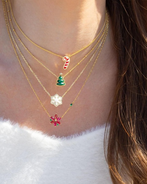 A close-up studio shot featuring four distinct gold-chain necklaces with Christmas-themed charms: a candy cane, a tree, a snowflake, and a red flower.