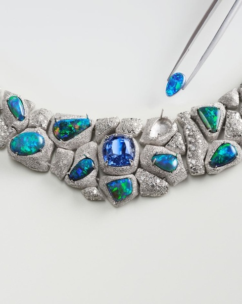 A high-end necklace is shown in a professional studio setting with a jeweler's tool placing an opal, highlighting the premium quality and detailed construction.