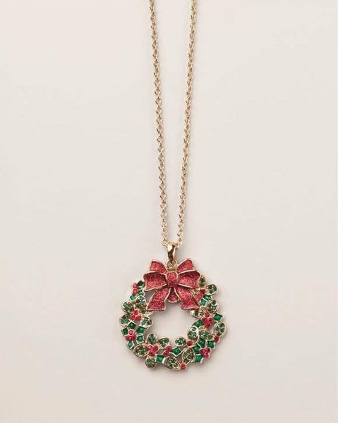 A gold chain necklace featuring a small, detailed Christmas wreath pendant with a red bow and green accents against a neutral background.