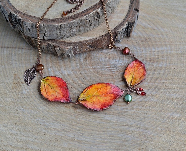 A close-up product shot of a delicate, hand-crafted autumn leaf necklace resting on rustic wood, capturing a warm seasonal aesthetic.