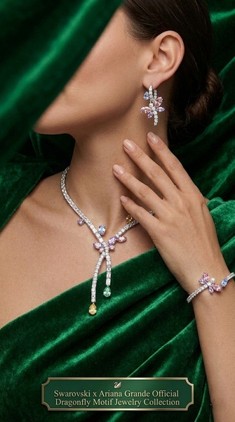 A close-up view of a model wearing a dragonfly-themed necklace and matching earrings against a deep green velvet background.