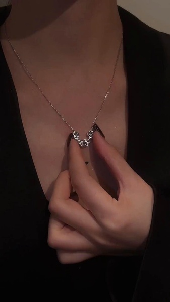 A close-up, 9:16 vertical video showing a hand gently unfolding a magnetic heart necklace into a four-leaf clover shape.