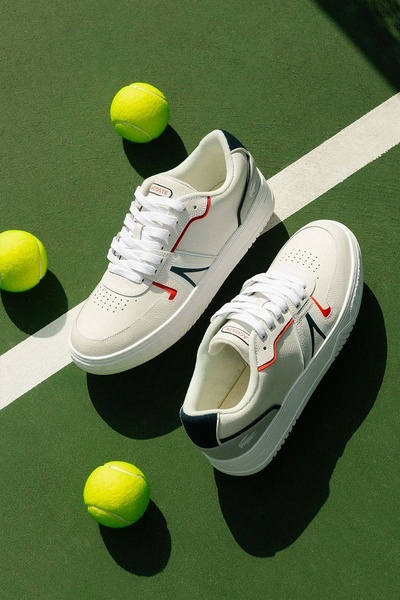 A high-angle product shot of two tennis shoes placed on a tennis court, framed by three tennis balls to create a clear, thematic visual narrative.