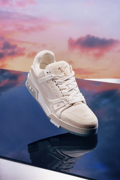 This creative features a single luxury sneaker suspended over a reflective surface against a soft, sunset-colored gradient sky.
