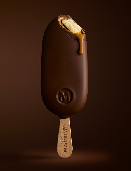 A high-contrast, close-up shot of an ice cream bar with a bite taken out, revealing a melting caramel center against a dark, minimalist background.