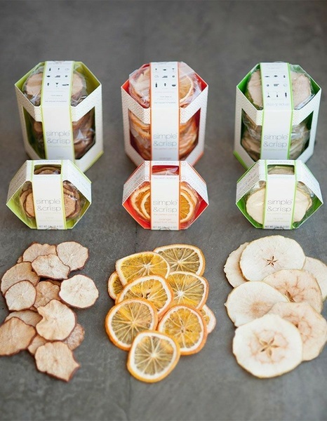 A clean, top-down product display showing three varieties of dehydrated fruit slices inside branded hexagonal packaging alongside the product itself.