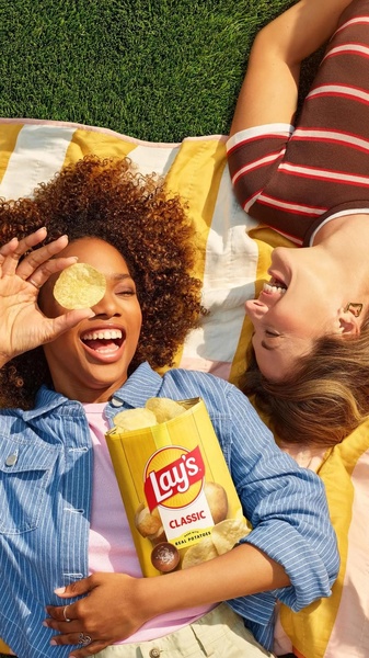 A high-angle shot of two people laughing on a picnic blanket with a bag of potato chips, using a lifestyle-focused visual hook to build brand affinity.