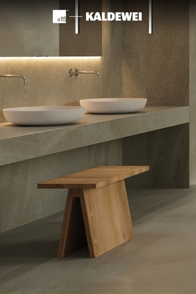 A high-end, clean architectural shot of a bathroom vanity with integrated stone sinks and a wooden bench, emphasizing a premium brand aesthetic.