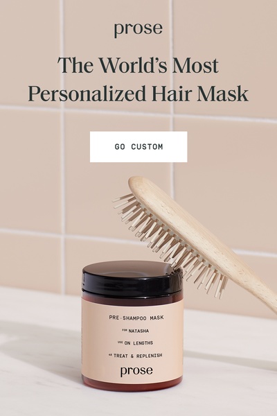 A clean, minimalist product shot of a personalized hair mask jar placed next to a wooden hair brush against a tiled backdrop.