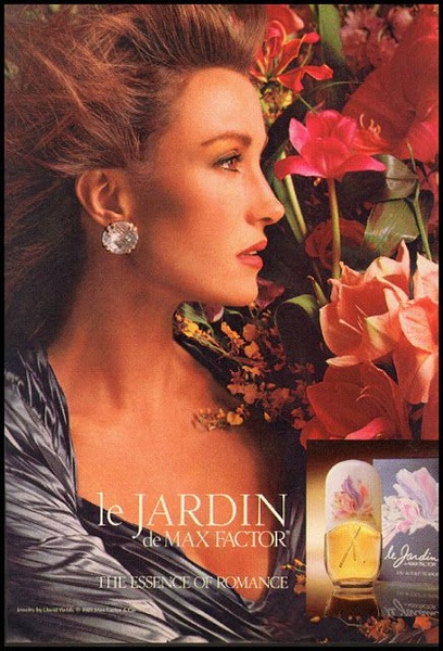 A high-end luxury advertisement featuring a woman surrounded by vibrant, oversized flowers with a bottle of the signature perfume in the foreground.