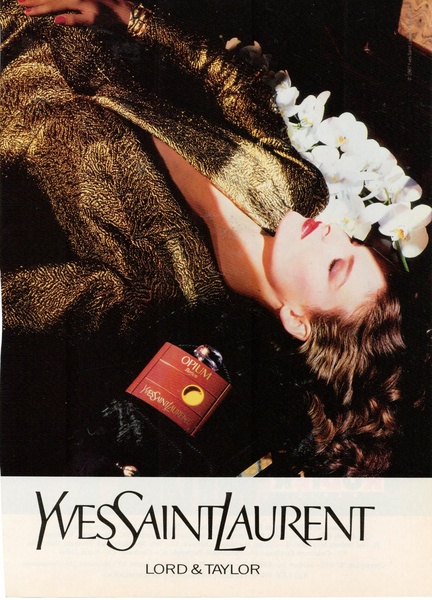 A high-end editorial shot featuring a perfume bottle resting near a model in a metallic gold jacket and white orchids.