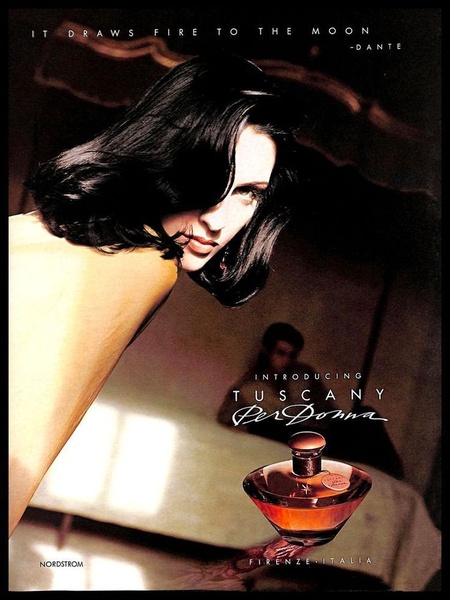 A high-fashion perfume ad featuring a dramatic, low-light setting with a woman leaning over a table toward a displayed perfume bottle.