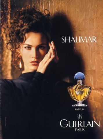 A sophisticated, warm-toned portrait featuring a model alongside the Shalimar perfume bottle, emphasizing high-end brand identity.