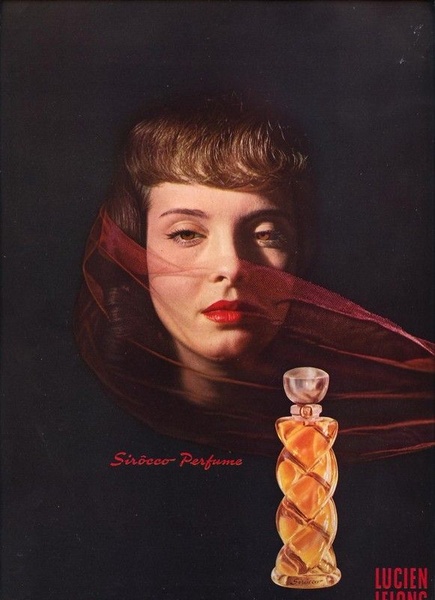A high-contrast, dramatic portrait featuring a model veiled in red gauze with the perfume bottle in the foreground.