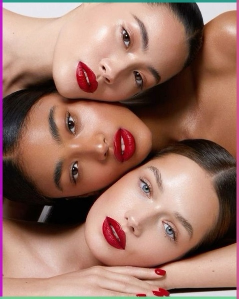 A striking close-up shot featuring three models with identical bold red lipstick, arranged in a tight triangular formation to draw immediate focus to the product.